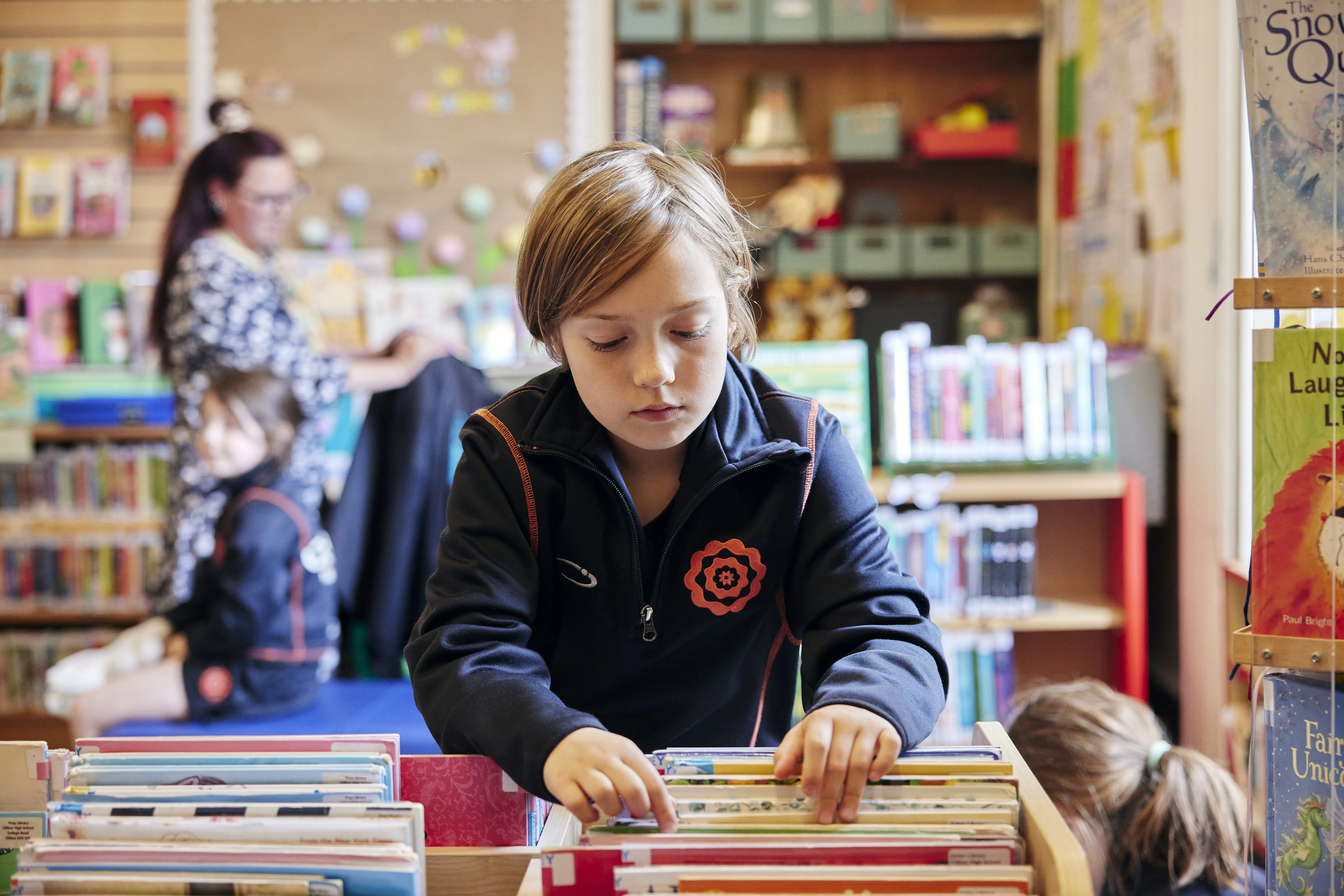 Pupil selecting a book in the Infant and Junior School Library at Clifton High School, surrounded by age-appropriate reading resources and colourful book displays.
