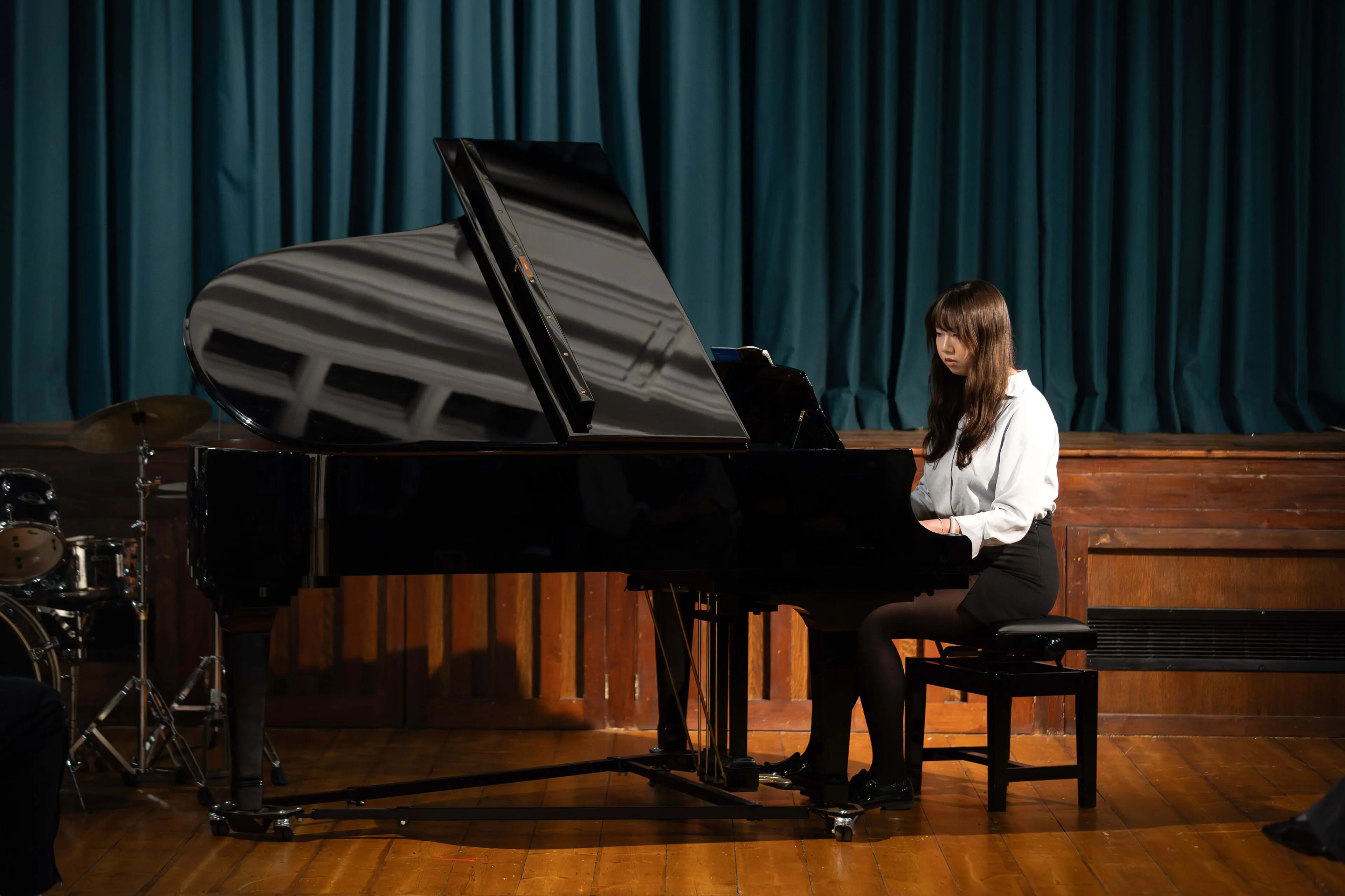 Pupil performing on a grand piano during a concert in the Main Hall at Clifton High School.